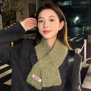 Nahaufnahme des grünen Strickschals mit flauschiger Textur und rosa Etikett in Stadtszene