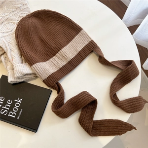 Detail of coffee and beige striped knit hat with long straps on a minimalist white table