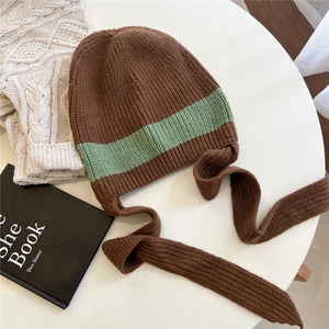 Close-up of a brown and green striped knit hat with long straps on a white table