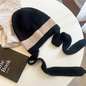 Close-up of knit earflap hat with contrast yellow stripe and long woven tassels