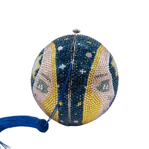 Detail of moon-shaped rhinestone clutch with artistic eye pattern and blue velvet tassel