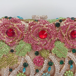 Detail showing crystal-encrusted pink roses and red gemstones on luxury gold clutch