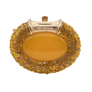 Macro detail of amber oval stone and yellow rhinestone pavé on a golden luxury clutch