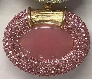 Macro detail of oval pink gemstone pendant with sparkling rhinestone halo and gold metal