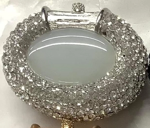 Macro detail of oval rhinestone clutch closure with large central cabochon and crystal pavé