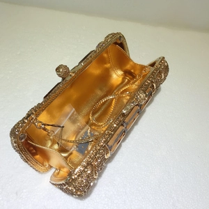 Dettaglio di pochette da sera dorata con strass, tracolla a catena e decoro di lusso