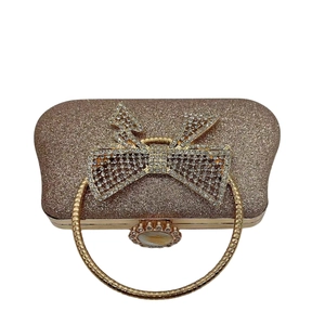 Detail of champagne gold sequin clutch bag with large rhinestone bow and metal ring handle
