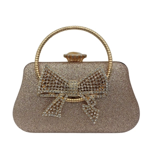 Macro view of champagne gold evening bag featuring rhinestone bow and metal handle