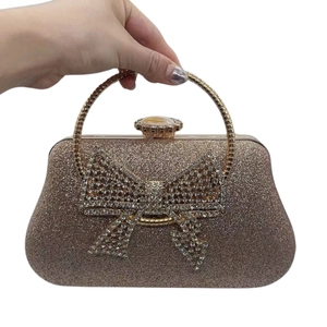 Detail of champagne gold evening clutch featuring a large rhinestone bow and metal handle