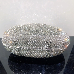 Detailed view of silver crystal encrusted oval clutch with metallic hinge on reflective surface