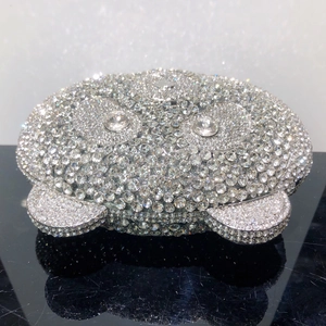 Macro detail of silver bear-shaped clutch with hand-set crystals on reflective surface