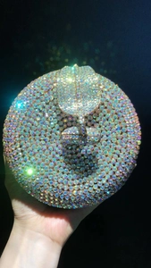 Close-up of a circular evening clutch bag with iridescent rhinestones in a hand-held view