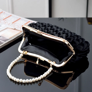 Detail of black satin pleated clutch showing pearl handle and gold metal frame closure