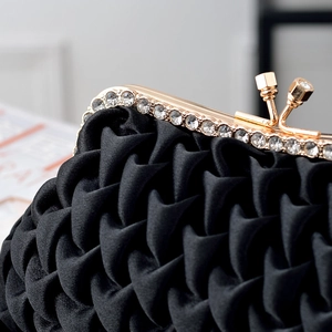 Close-up of elegant pleated black satin clutch with sparkling rhinestone and gold clasp
