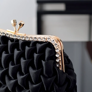 Detail of black satin pleated clutch featuring a gold rhinestone-inlaid metal frame and clasp