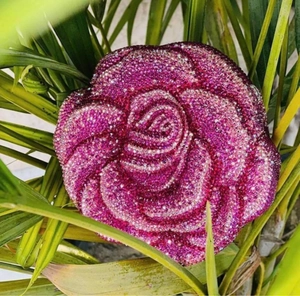 Close-up of pink rose flower clutch purse with sparkling rhinestones on green leaves