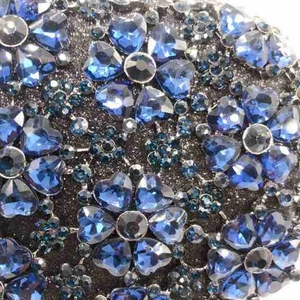 Macro detail of blue heart crystals and dark gray glitter metal on evening clutch bag