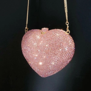 Detail of pink heart crystal evening bag with golden chain on black background
