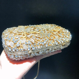 Détail d'une pochette dorée avec motifs floraux en strass et bandoulière en chaîne fine