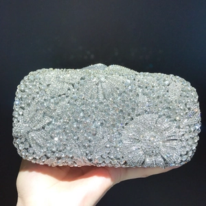 Close-up of a silver floral crystal clutch bag held by hand against a black background