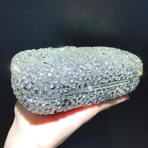 Macro detail of silver clutch bag with sparkling crystals and metal clasp on black backdrop
