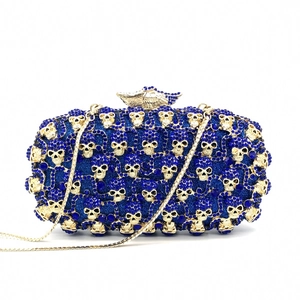 Détail d'une pochette en strass bleus avec motifs crânes dorés et fermoir ailé