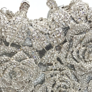 Macro detail of silver evening clutch showing intricate rose pattern with inset rhinestones