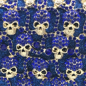 Détail de strass bleus sur pochette de soirée tête de mort dorée avec fond scintillant