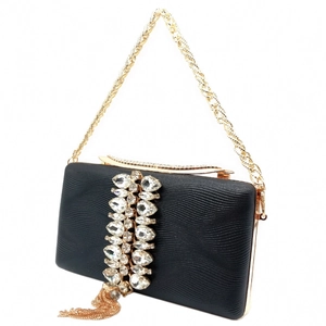 Macro detail of the sparkling rhinestones and golden tassels on a black evening clutch