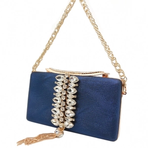 Detail of navy blue evening clutch featuring wavy texture, crystals, and gold chain tassel
