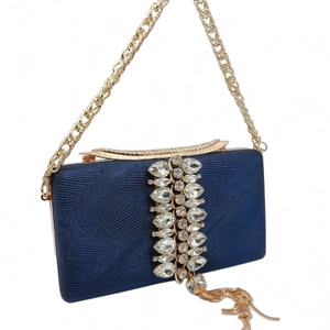 Detail of dark blue evening clutch with wavy texture, rhinestones, and gold metal tassels