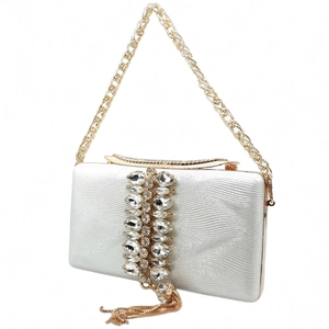 Detail of white evening clutch featuring wavy texture, crystals and golden fringe tassels