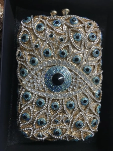 Makroaufnahme der Evil-Eye-Abendtasche mit gold-blauen Kristallen in einer Geschenkbox