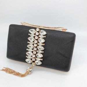 Detail of black evening clutch with wave texture, sparkling crystals and gold tassel