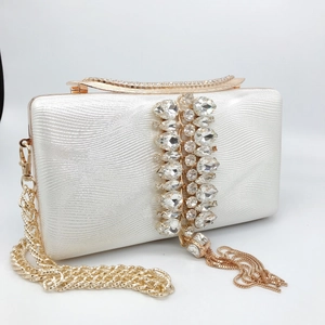 Close-up of cream evening clutch with wavy texture, sparkling rhinestones and gold tassels