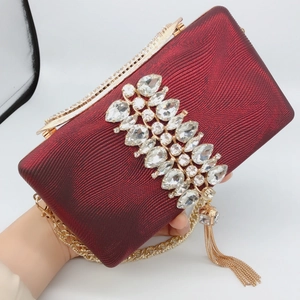 Detail of burgundy evening clutch with rhinestones floral ornament and metallic chain