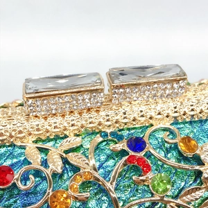 Macro detail of luxury gold floral metal clutch with multicolor crystals and emerald base