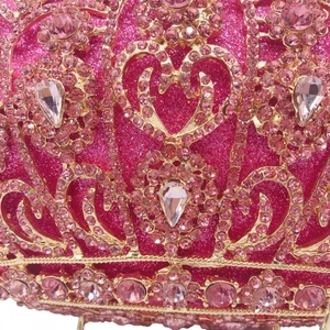 Macro detail of pink sparkling rhinestones and golden crown hollow metal frame on evening clutch