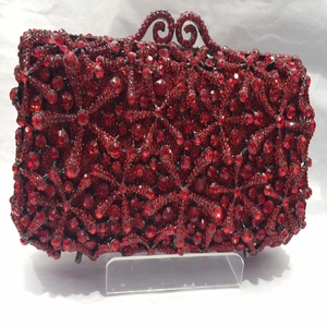 Detail showing red crystal starburst pattern and black metal floral clasp on evening bag
