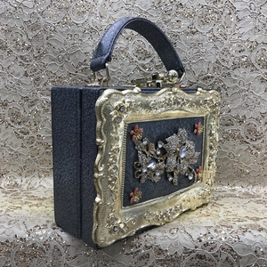 Detail of dark grey evening bag featuring ornate gold baroque frame and diamond floral inlay