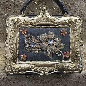 Detailed view of luxury evening clutch featuring rhinestone flowers and gold embossed frame
