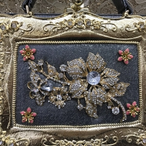 Close-up of golden embossed frame with rhinestone flowers and pink enamel on dinner bag