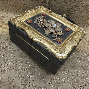Detailed view of luxury evening clutch with gold embossed frame and rhinestone flower