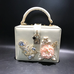 Détail du sac à main boîte crème avec fleur en tissu rose et boucle strass paon