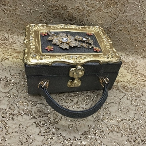 Macro detail of rhinestone floral pattern and gold embossed frame on vintage handbag