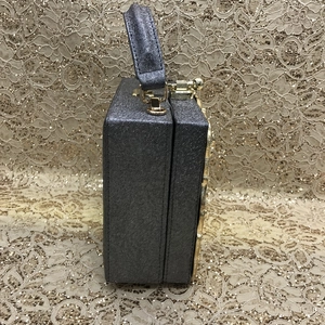 Side view of silver glitter box evening bag with gold metal latch and handle detail