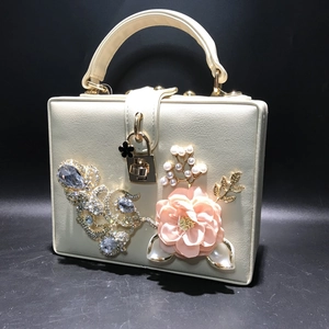 Détail du sac boîte crème avec fleur 3D, perles et strass sur un fond noir profond