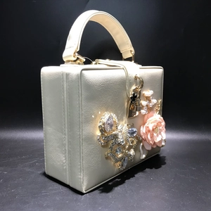 Gros plan sur pochette rigide beige avec fleur 3D rose, perles et détails en strass