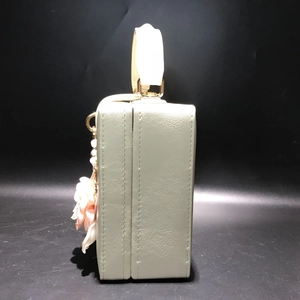 Détail d'un sac boîte beige élégant avec accent floral 3D et poignée supérieure