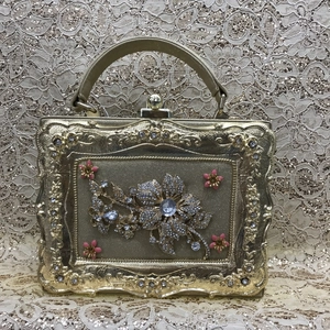 Detail of golden evening bag featuring rhinestone floral bouquets and pink 3D flowers